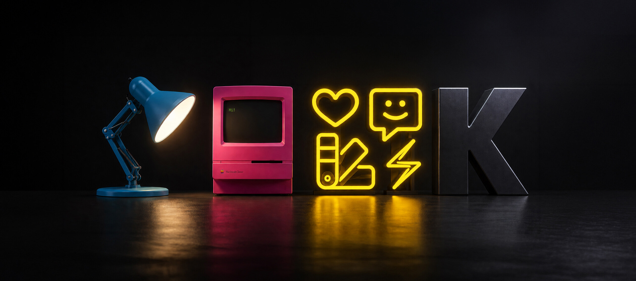 A desk lamp, a pink Macintosh Classic, glowing neon icons, and a large letter K on a dark desk